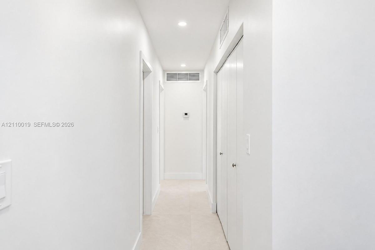 Hallway featuring neutral tile flooring, recessed lighting, and white bi-fold closet doors