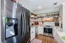 Kitchen featuring stainless steel appliances, stone-look countertops, white cabinetry with crown molding, natural wood-finish open shelving, and a whi