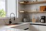 White cabinetry with black recessed pulls, stone-composite countertops with matching full-height backsplash, wall-mounted wood floating shelving, and 
