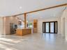Open-concept interior featuring vaulted ceilings with exposed wood beams, large-format tile flooring, a kitchen island with wood-finish cabinetry, bui