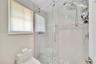 Walk-in shower featuring a glass sliding door, polished metal rain showerhead with handheld attachment, horizontal white tile walls with a decorative 