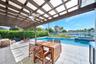 Covered patio featuring a wood-beam pergola, integrated ceiling fans, stone paver flooring, an in-ground pool, and a raised spillover spa