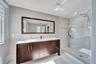 Double vanity with rectangular undermount sinks and light-toned solid surface countertop, wood-finish cabinetry with metallic hardware, and walk-in gl