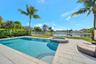 Swimming pool with integrated spillover spa, tiled deck, perimeter fencing, and mature palm trees