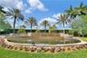 Stone-accented water feature, curated perimeter landscaping, mature palm trees, manicured turf, and tiered stone masonry walls