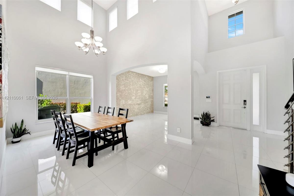 Double-height ceiling, polished tile flooring, multi-tier chandelier, stone-texture wall feature, and large windows with integrated transom lighting
