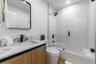 Modern bathroom featuring a wood-finish vanity, stone-surfaced countertop, frameless glass shower enclosure, matte black fixtures, and a rectangular m