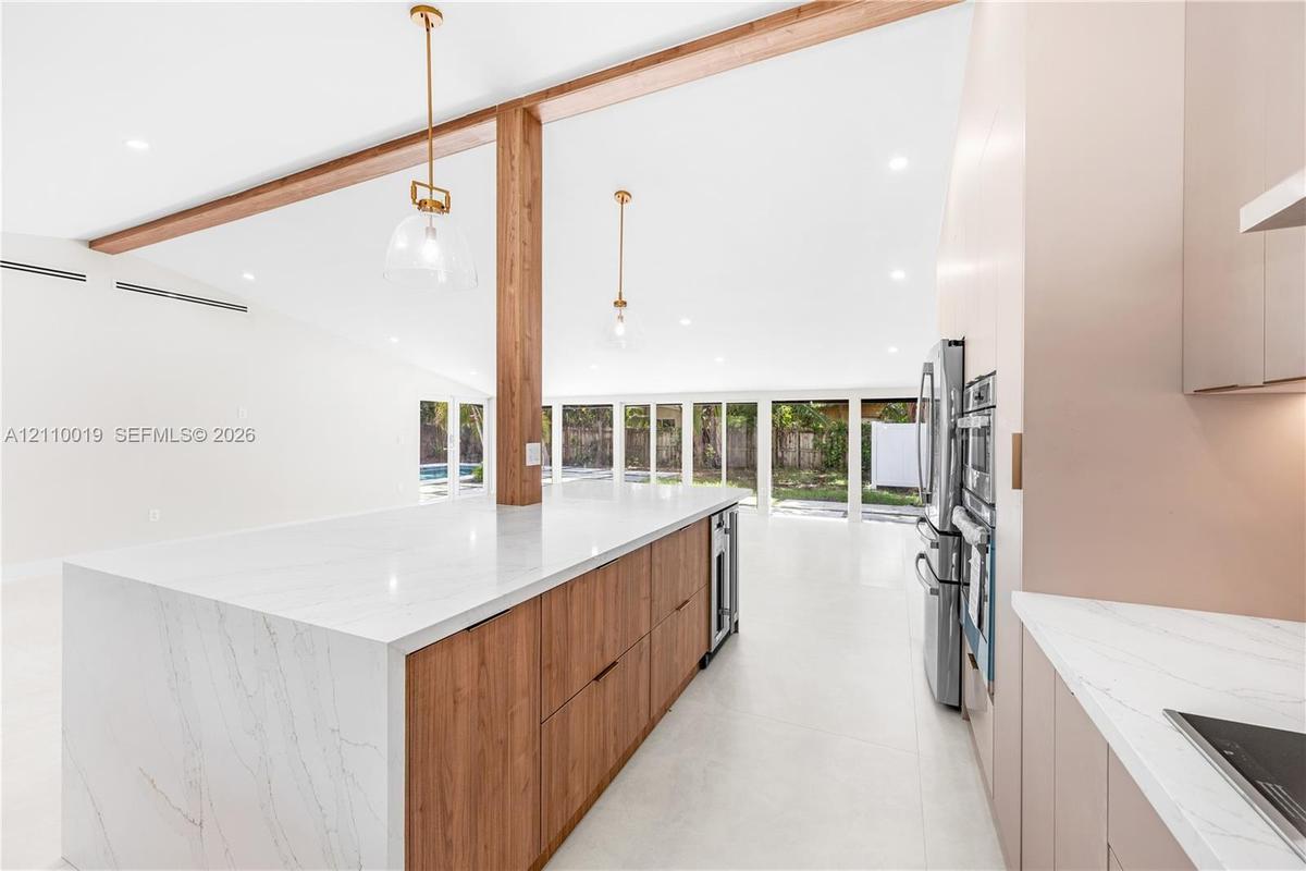 Kitchen featuring a waterfall-edge stone countertop, wood-finish cabinetry, exposed wood ceiling beams, pendant lighting, and stainless steel built-in