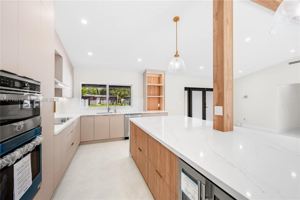 Kitchen featuring flat-panel cabinetry, a spacious stone-surfaced island, integrated stainless steel appliances, a structural wood pillar, and recesse