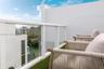 Private balcony featuring glass panel railing, white exterior stucco walls, and artificial turf flooring