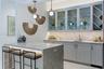 Custom cabinetry with glass-front display doors and wine storage, stone-topped island with waterfall edge, herringbone-patterned tile backsplash, unde
