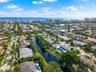 Aerial perspective of a coastal residential community featuring a network of canals, private swimming pools, mature palm trees, and residential archit