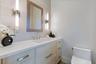 Custom vanity with quartz countertop, undermount sink, stone-finish wall cladding, dual vertical wall-mounted light fixtures, and framed mirror