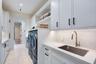 Laundry area featuring Shaker-style cabinetry, quartz countertops, a stainless steel undermount sink with a gooseneck faucet, light-toned stone-finish
