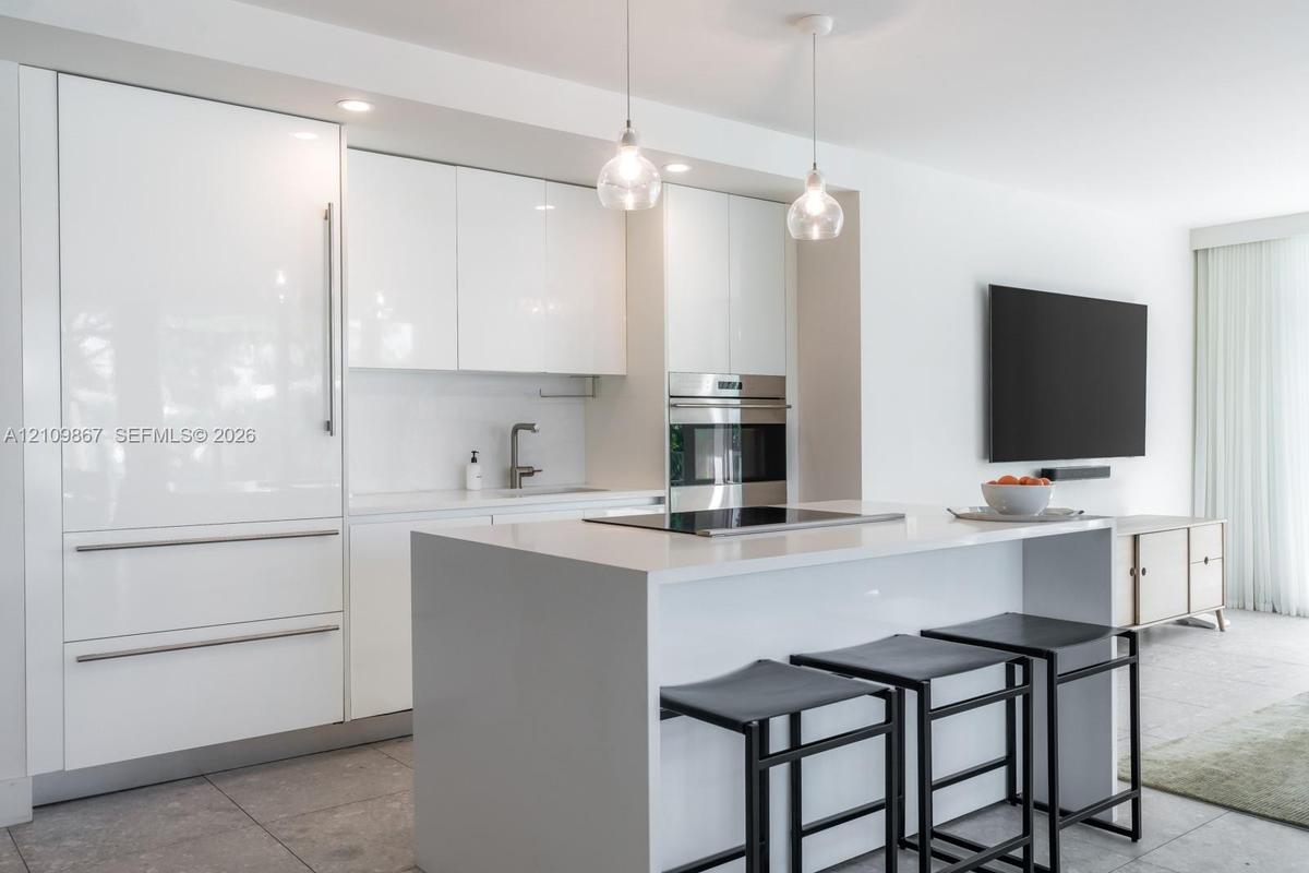 Modern kitchen featuring high-gloss cabinetry, a central island with a solid-surface countertop, integrated appliances, and pendant lighting