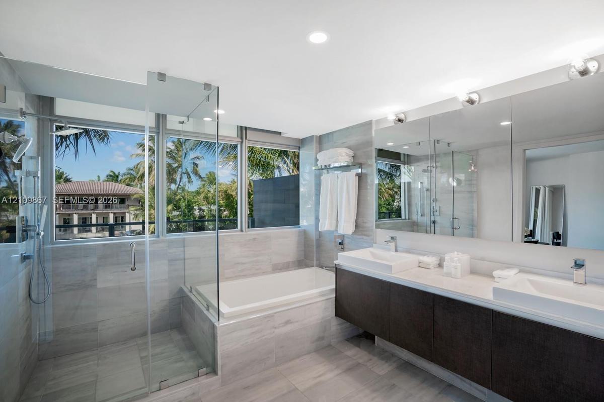 Bathroom featuring a floating dual vanity with rectangular vessel sinks, a glass-enclosed shower, a deep soaking tub, and floor-to-ceiling windows