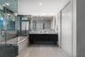 Floating dual-sink vanity with a countertop, expansive wall-mounted mirror, glass-enclosed soaking tub, and tile flooring
