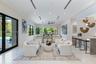 Open-concept living area featuring large-format stone flooring, recessed linear lighting, black-framed windows, integrated wet bar with stone countert