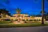 Single-story residence featuring light-toned stucco exterior, stacked stone facade accents, dark metal roof, multiple transom windows, and paved stone
