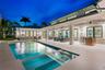 Covered outdoor patio with stone tile flooring, built-in outdoor kitchen, swimming pool with integrated spa, and expansive multi-panel sliding glass d