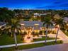 Modern residence featuring a standing-seam metal roof, paver driveway, manicured lawn, stone-surface entryway, and mature palm landscaping