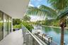 Covered balcony featuring tile flooring and a glass panel railing, overlooking a waterway with a private dock and mature palm trees