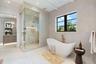 Freestanding soaking tub with a wall-mounted faucet, glass-enclosed shower featuring built-in shelving, large-format tile flooring, and plank-style ce