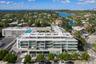 Multi-story residential complex featuring glass-railed balconies, a rooftop swimming pool, modern concrete exterior architecture, and mature landscapi