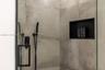 Shower enclosure featuring large-format grey tile, matte black shower hardware, a hand-held shower sprayer, and a built-in recessed storage niche