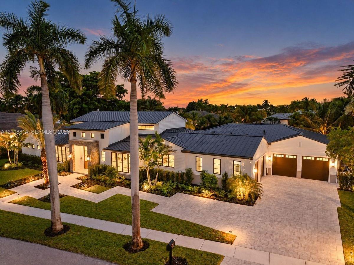 Modern architectural exterior featuring a metal roof, stone facade accents, multi-pane windows, and a paved driveway leading to an attached two-car ga