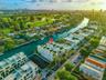 Aerial perspective of a multi-story waterfront property featuring canal frontage, rooftop terraces, white exterior cladding, and proximity to a golf c