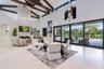 High-ceilinged living area featuring exposed wood ceiling beams, a floor-to-ceiling stone-clad fireplace, built-in shelving, and expansive multi-panel