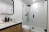 Bathroom featuring a wood-finish vanity with a stone-surface countertop, a frameless glass shower enclosure, matte black fixtures, a rectangular vanit