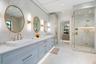 Dual-basin vanity featuring quartz countertops, large-format tile wall cladding, glass-enclosed walk-in shower with integrated recessed shelving, and 