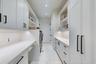 Custom cabinetry with matte black hardware, stone countertops, integrated under-cabinet lighting, and light-toned tile flooring