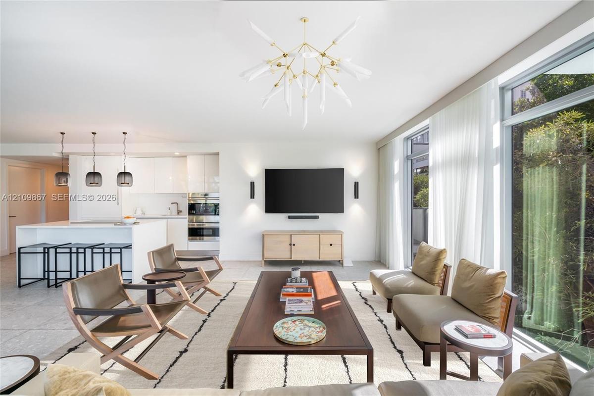 Open-concept interior featuring floor-to-ceiling windows, white cabinetry, a kitchen island, and custom brass-finish chandelier