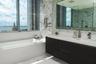 Floating dark cabinetry with an integrated countertop and sink, wall-spanning vanity mirror, floor-to-ceiling stone wall cladding, deep soaking tub, a