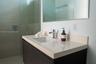 Floating vanity with a light-toned countertop, rectangular undermount sink, chrome faucet, wall-mounted mirror, and glass-enclosed shower featuring ho
