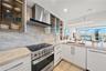 Gourmet Kitchen featuring Taj Mahal Quartzite countertops, full-height Taj Mahal stone backsplash, glass-front cabinetry with interior lighting, Fishe