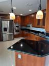Kitchen featuring wood cabinetry, black countertops, stainless steel built-in double oven, stainless steel refrigerator, and pendant lighting