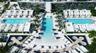 Multi-level swimming complex featuring expansive sun decks, symmetrical water features, integrated palm tree landscaping, and uniform hardscaping