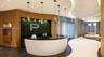 Curved reception desk featuring a high-contrast white base with textured floral-motif paneling and a dark stone countertop, set against a preserved gr