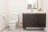 Floating vanity with a dark textured cabinet, integrated countertop, chrome single-handle faucet, and white tile flooring with grey veining