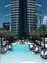 High-rise tower with floor-to-ceiling glass facade and wraparound balconies, featuring a swimming pool, integrated poolside cabanas, and manicured pal