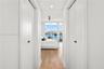 Master bedroom hallway with dual bifold closet doors, wood-finish flooring, recessed LED lighting, and floor-to-ceiling windows with views of the down