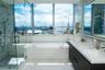 Floor-to-ceiling windows, glass-enclosed walk-in shower with stone tile wall, built-in soaking tub, and dark wood-finish vanity with white countertop