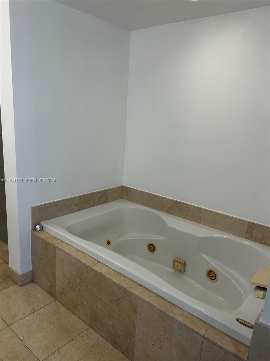 Jetted soaking tub with integrated controls, surrounded by neutral-toned stone tile wainscoting and coordinating floor tile