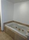 Jetted soaking tub with integrated controls, surrounded by neutral-toned stone tile wainscoting and coordinating floor tile