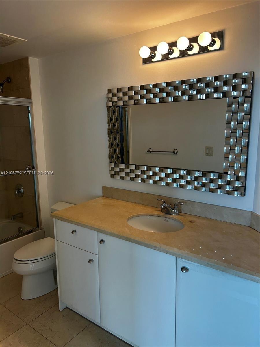 Bathroom vanity featuring white cabinetry, a neutral-toned stone-finish countertop, an oval undermount sink, a metallic basket-weave framed mirror, an