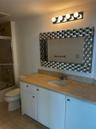 Bathroom vanity featuring white cabinetry, a neutral-toned stone-finish countertop, an oval undermount sink, a metallic basket-weave framed mirror, an